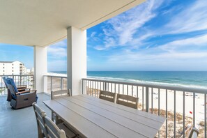 Een balkon met uitzicht op het strand en de oceaan, een tafel, stoelen en een rieten stoel.