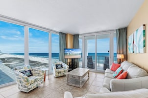 A spacious living room with a large window overlooking a beach, a television, and a sofa.
