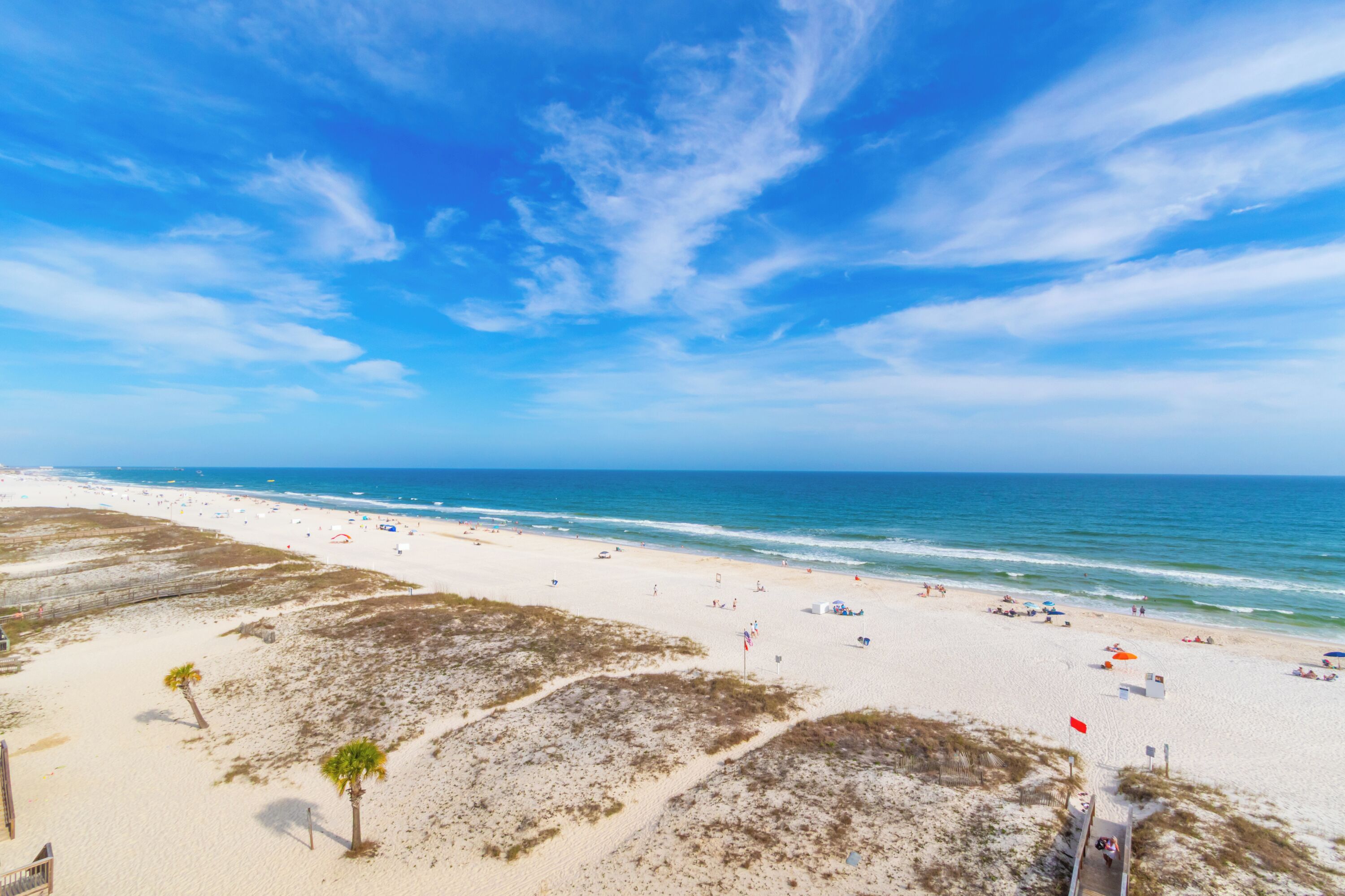 Une plage avec des dunes de sable, un ciel dégagé et l’océan.