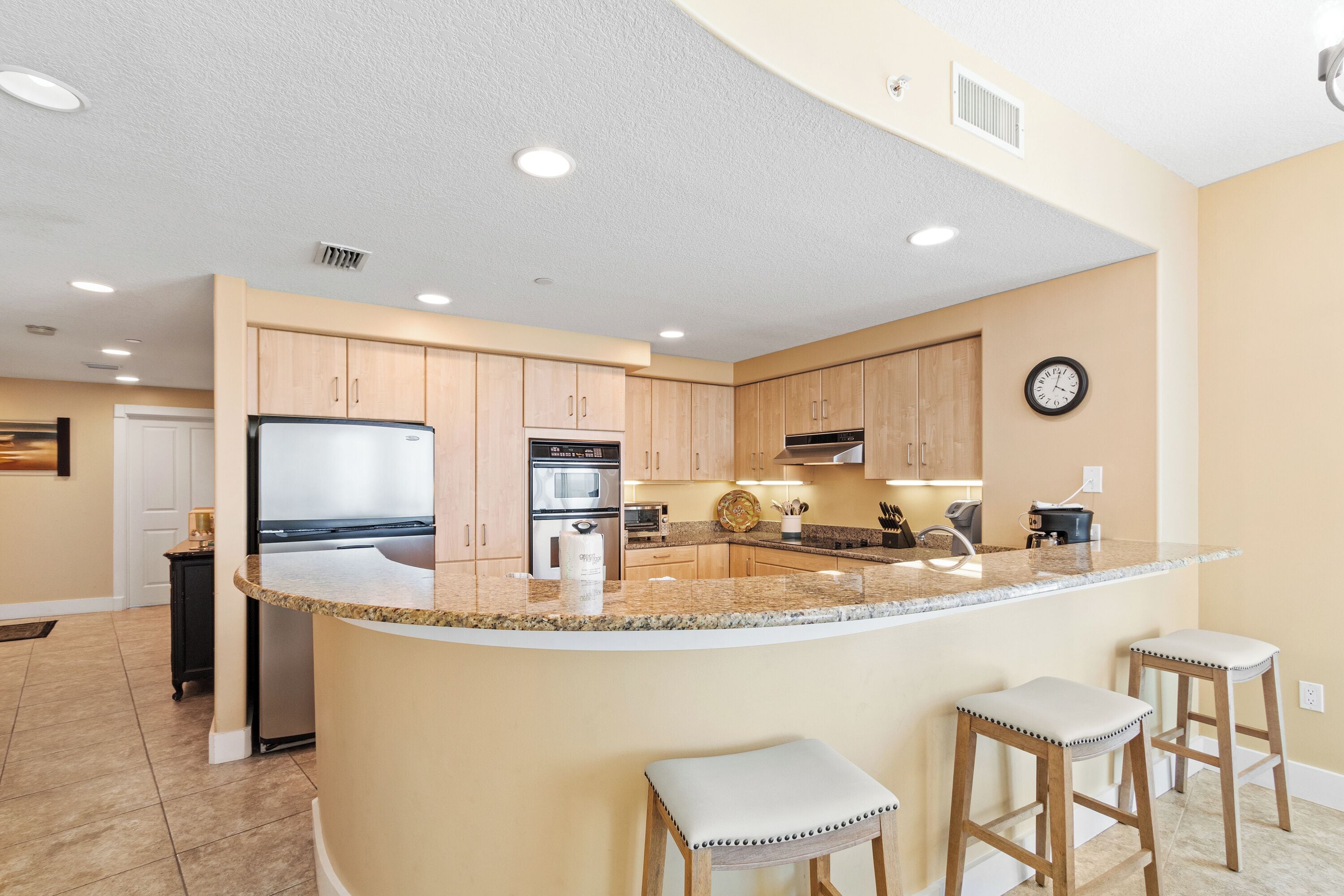 A kitchen with a central island, wooden cabinets, stainless steel appliances, and a clock on the wall.