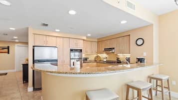 A kitchen with a central island, wooden cabinets, stainless steel appliances, and a clock on the wall.