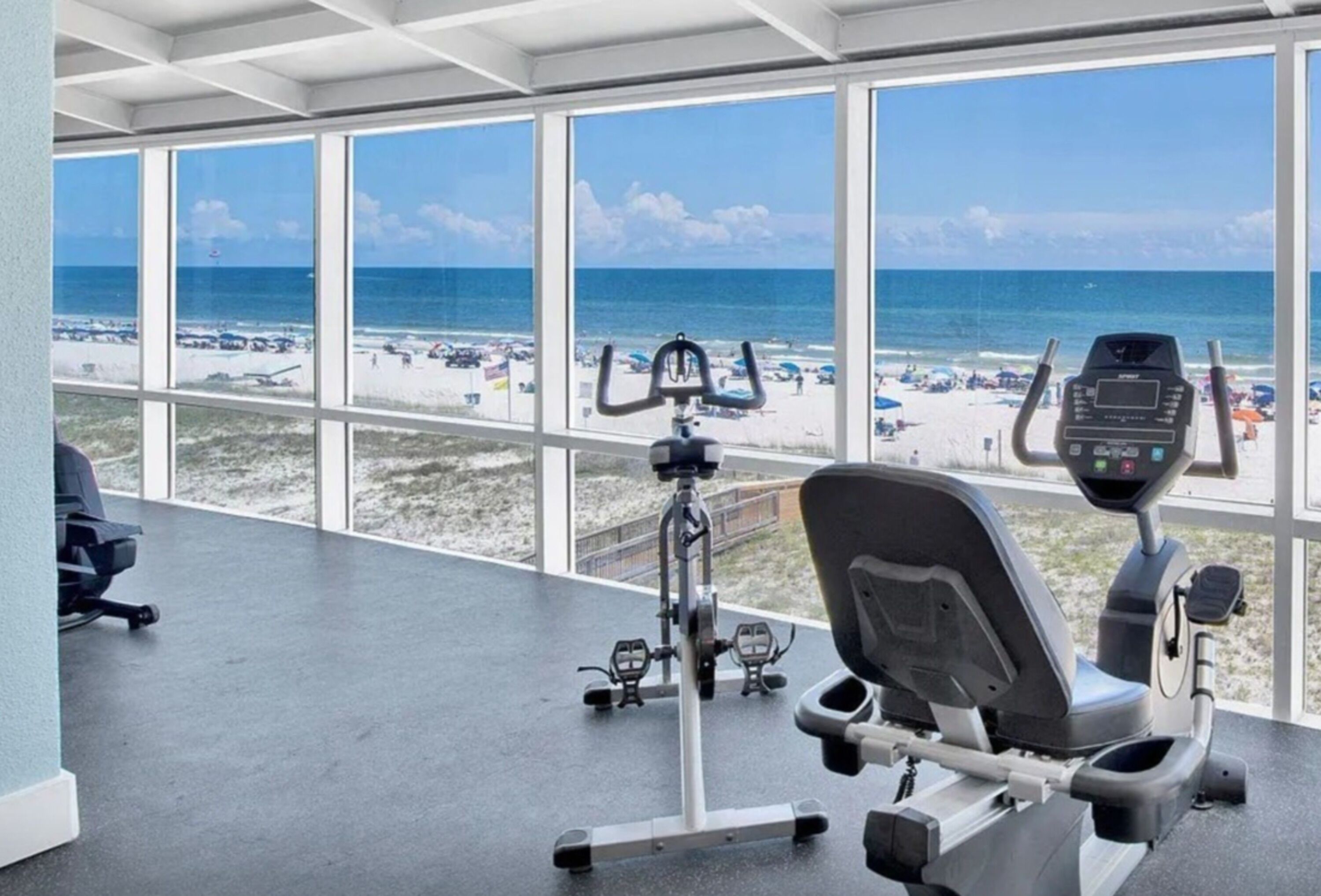 A gym with large windows overlooking a beach.