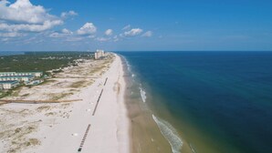 An aerial view of a beach with a long stretch of sand, a pier, and buildings along the coastline. - Modern condo with Gulf view, shared pool - walk to the beach (Fort Morgan)