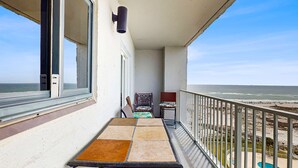 Ein Balkon mit Tisch und Stühlen mit Blick auf Strand und Meer.