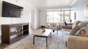 Un salon moderne doté d’un téléviseur à écran plat, d’un meuble de rangement en bois, d’une table basse, d’un canapé et offrant une vue sur l’extérieur grâce à de grandes fenêtres.