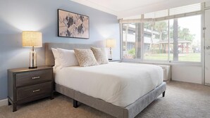 Une chambre à coucher comprenant un lit, deux tables de chevet, une commode, une fenêtre avec vue et une œuvre d’art accrochée au mur.