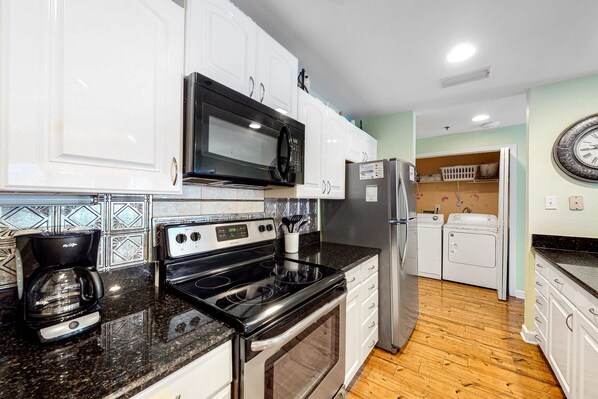 A kitchen with white cabinets, a black microwave, a stainless steel refrigerator, a coffee maker, and a washing machine. - Adorable Beach Condo W Shared Pool, Gulf Views, Private Balcony & WiFi (Fort Morgan)