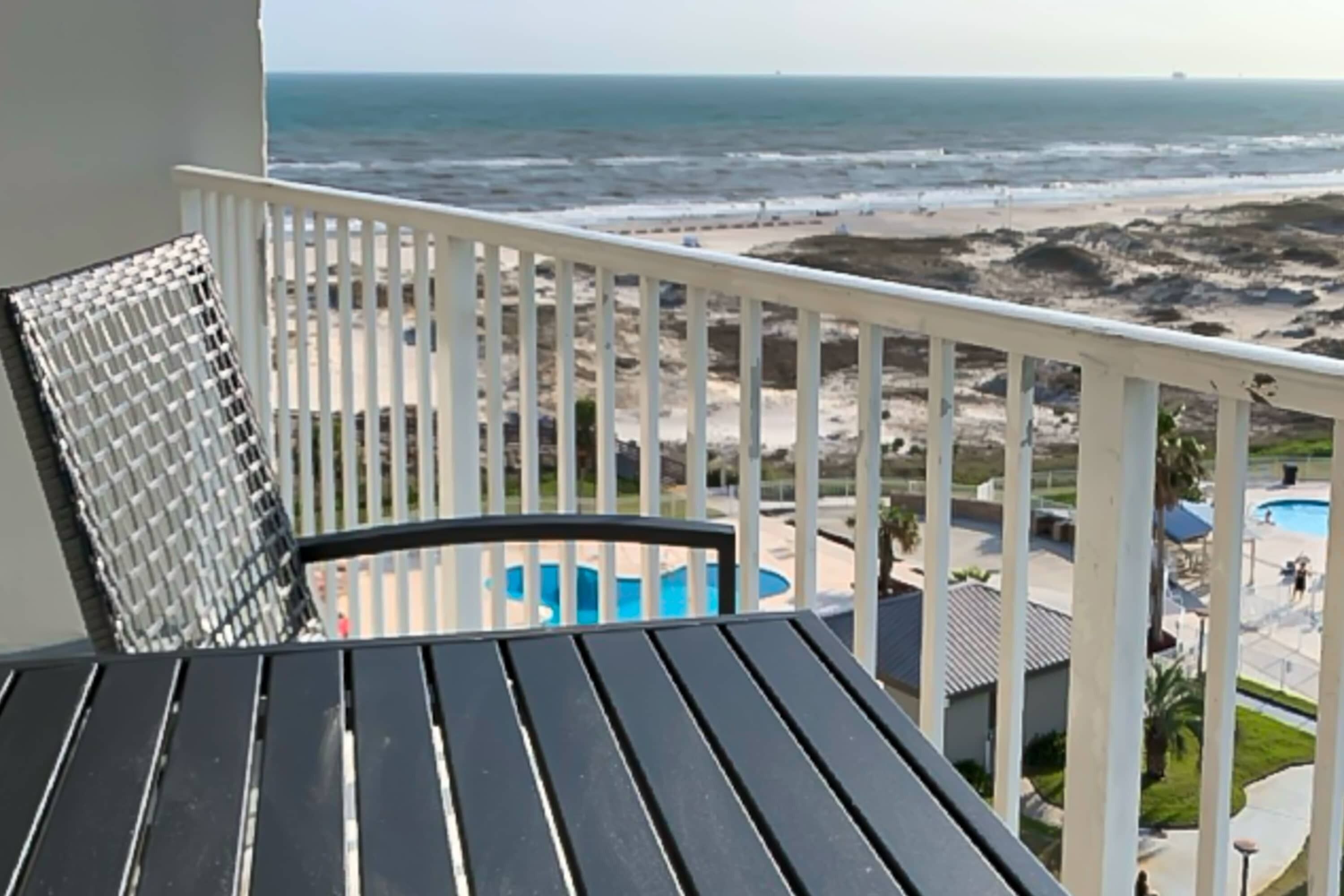 A balcony with a view of the beach and a pool.