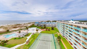 Ett hotell med flera våningar, en tennisbana, en pool och utsikt över stranden.