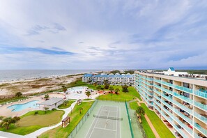 Ein Hotel mit mehreren Stockwerken, einem Tennisplatz, einem Pool und Blick auf den Strand.