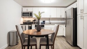 Une cuisine moderne avec des armoires blanches, des appareils en acier inoxydable et une table à manger avec des chaises.