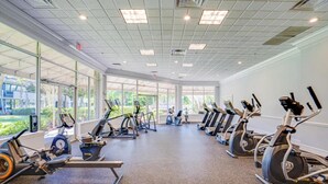 Une salle de sport équipée de vélos d’appartement et de tapis de course, dotée de grandes fenêtres et présentant un design moderne et épuré.
