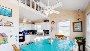 Een keuken met witte kasten, een eettafel met een blauwe tafelkleed en een plafondventilator.