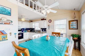 A kitchen with white cabinets, a dining table with a blue tablecloth, and a ceiling fan.