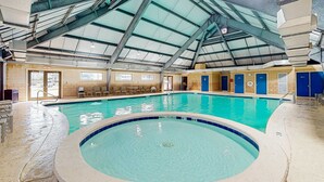 En inomhuspool med högt tak, blå kakelplattor längs kanterna och ett takfönster.