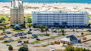 Een groot hotel met meerdere verdiepingen, een parkeerplaats en een strand op de achtergrond.