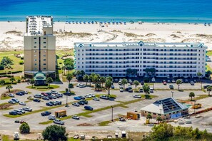 Ein großes Hotel mit mehreren Etagen, einem Parkplatz und einem Strand im Hintergrund.