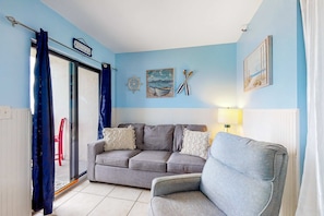 Una habitación con un sofá gris, una pared azul, una ventana con cortinas, una silla roja y decoración temática náutica.