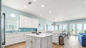 A spacious kitchen with white cabinetry, a central island, and a dining area with a view. - Completely renovated oceanfront home with shared outdoor pool, views, & balcony (Fort Morgan)