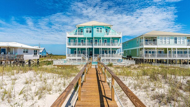 A beachfront property with a wooden boardwalk leading to a multi-story building with balconies. - Completely renovated oceanfront home with shared outdoor pool, views, & balcony (Fort Morgan)