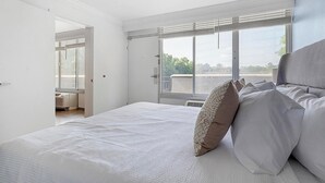 Un dormitorio con una cama grande, una ventana con persianas y vistas a zonas verdes.