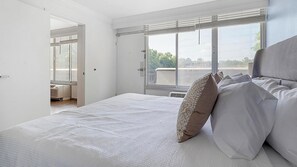 A bedroom with a large bed, a window with blinds, and a view of greenery outside. - Landing | Spectacular 1BD, Clubhouse, Gym (Kissimmee)