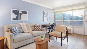Una sala de estar con sofá, sillón, mesa de centro y obras de arte en las paredes.