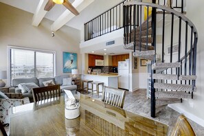 A spacious living area with a dining table, a kitchen with a modern design, and a spiral staircase. - Bright corner condo steps from the beach with pools, hot tubs & tennis (Fort Morgan)