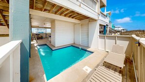En pool på taget med udsigt over havet, et overdækket siddeområde og en bygning med balkon.