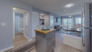 Eine moderne Küche mit einer zentralen Kochinsel, einem Essbereich mit Tisch und Stühlen sowie ein sichtbares Badezimmer mit Dusche.