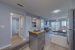 A modern kitchen with a central island, a dining area with a table and chairs, and a visible bathroom with a shower. - Gulf-view condo near Kiva Dunes with pool, hot tub, & gym - snowbird's delight (Fort Morgan)