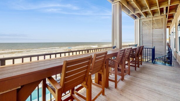 A wooden deck with chairs overlooking a beach. - Luxury Beachfront Duplex in Fort Morgan | Pool, Elevator and Wedding-Friendly (Fort Morgan)