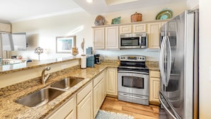 A kitchen with granite countertops, stainless steel appliances, and light-colored cabinetry. - Ocean-view condo with heated pool, hot tub & rooftop terrace - walk to beach (Fort Morgan)