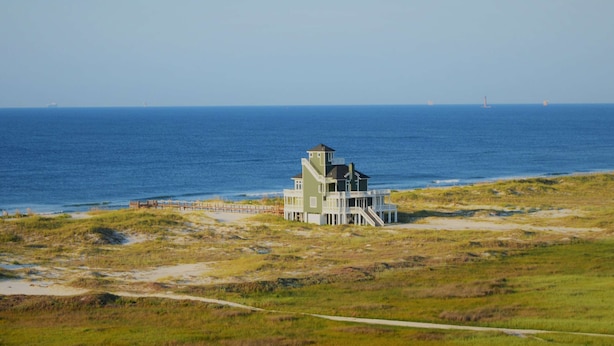 A coastal house with a beach view, a pier, and a lighthouse in the distance. - Ocean-view condo with heated pool, hot tub & rooftop terrace - walk to beach (Fort Morgan)