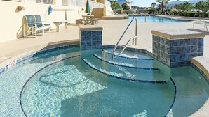 A swimming pool with clear water, a lifeguard stand, lounge chairs, and a sunbed. - Ocean-view condo with heated pool, hot tub & rooftop terrace - walk to beach (Fort Morgan)