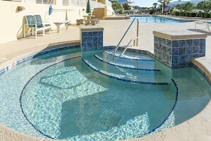 Ein Schwimmbecken mit klarem Wasser, einem Rettungsschwimmerstand, Liegestühlen und einer Sonnenliege.