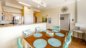 A dining area with a wooden table, teal chairs, and a decorative centerpiece. - Ocean-view condo with heated pool, hot tub & rooftop terrace - walk to beach (Fort Morgan)