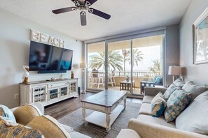 Ein Wohnzimmer mit Flachbildfernseher, Deckenventilator, großer Schiebeglastür zu einem Balkon und einem weißen Schrank.