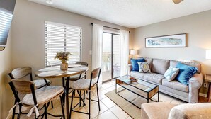 A living room with a sofa, coffee table, dining table with chairs, and a ceiling fan. - Renovated Gulf Front Condo with WiFi, Multiple Pools, & Beach Access (Fort Morgan)