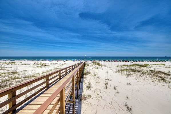 A wooden boardwalk leading to a beach with sand dunes and a clear blue sky. - Duplex home with two-level deck, beach access, hot tub, & balcony (Fort Morgan)