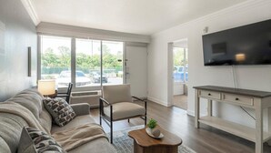 Sala de estar moderna com sofá, poltrona, mesa de centro, TV e vista para o exterior.