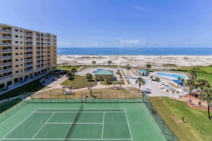 Een meerhoog hotel met een tennisbaan, zwembad en uitzicht op het strand.