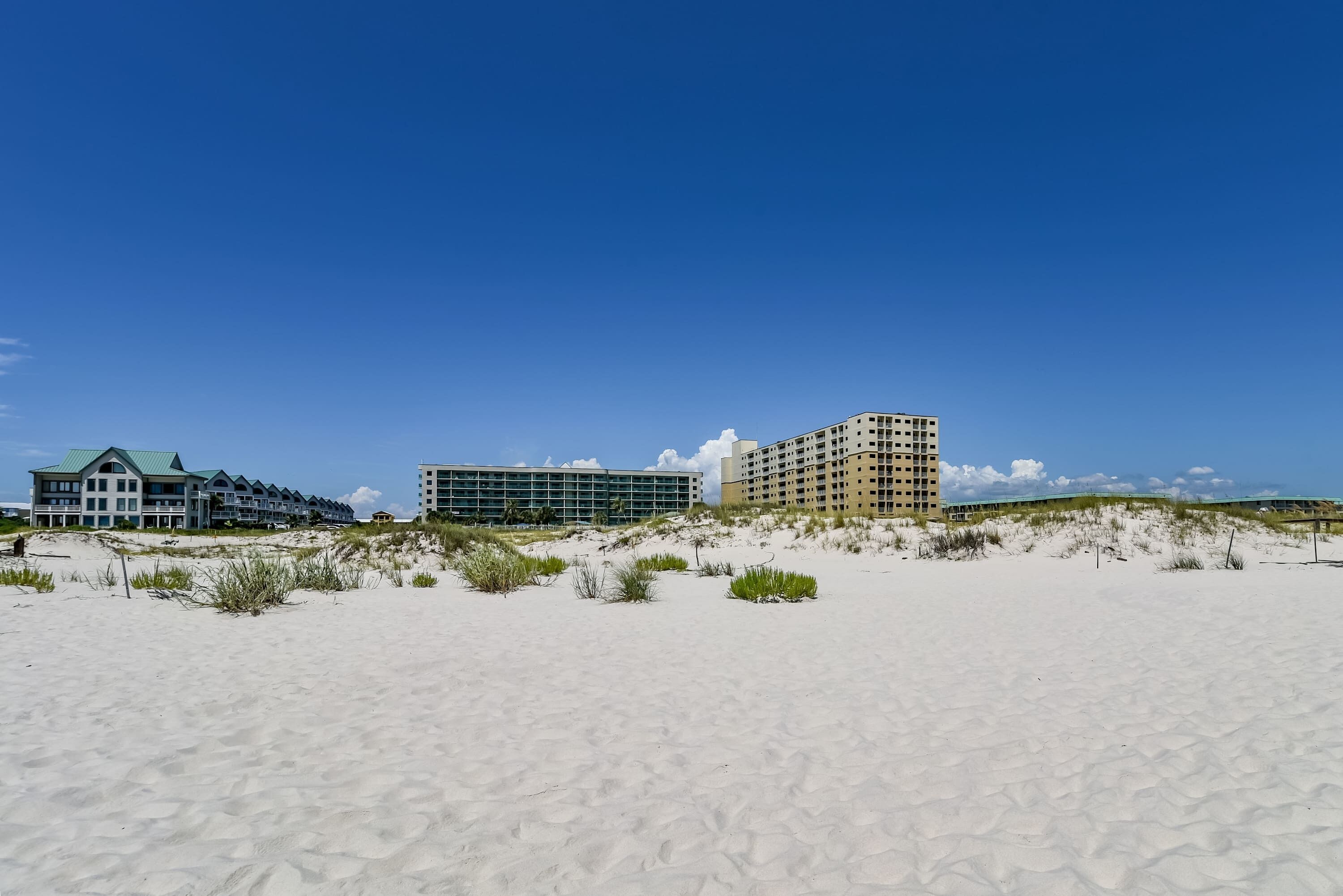 A beachfront hotel with multiple buildings, sandy beach, and dunes.