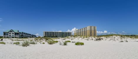 A beachfront hotel with multiple buildings, sandy beach, and dunes.