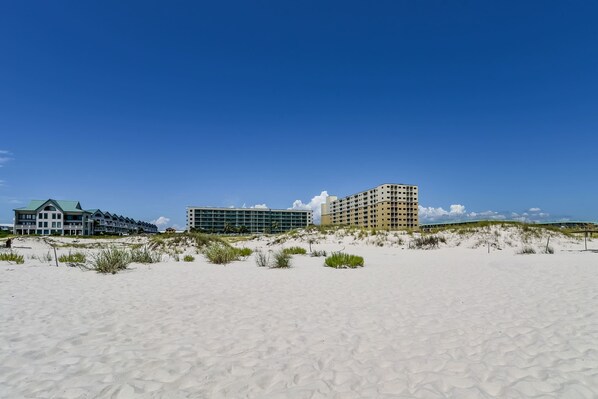 A beachfront hotel with multiple buildings, sandy beach, and dunes. - Condo with Gulf-facing balcony, shared pool, hot tub, gym (Fort Morgan)