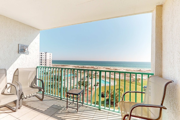 Varanda com cadeiras, uma mesa pequena e vista para a praia e oceano.