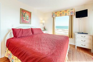A bedroom with a bed, a nightstand, a television, and a window with a view of the beach. - Gulf-front condo with balcony, shared pool, hot tub, & beach access (Fort Morgan)