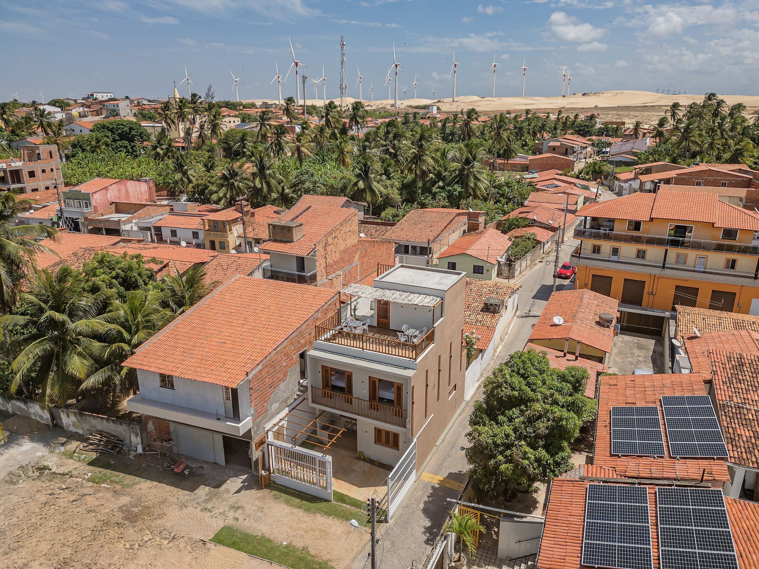 Uma área residencial com telhados vermelhos, uma combinação de edifícios térreos e com vários andares, e algumas turbinas eólicas à distância.
