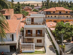 A multi-story building with a balcony, a gated entrance, and a visible staircase. - Casa Ladomar em Mundau por Carpediem (Trairi)