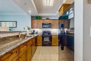 A kitchen with granite countertops, wooden cabinets, a black stove, a microwave, and a refrigerator.